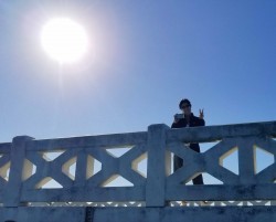 Image depicts a woman standing on bridge holding up a peace sign