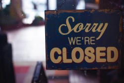 Image depicts an aging sign hanging in a window reading "Sorry We're Closed"