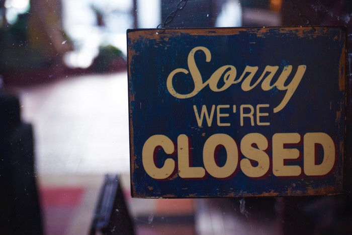 Image depicts an aging sign hanging in a window reading "Sorry We're Closed" 