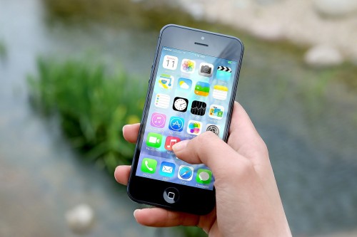Image depicts a hand holding an iphone with the screen on showing numerous app icons